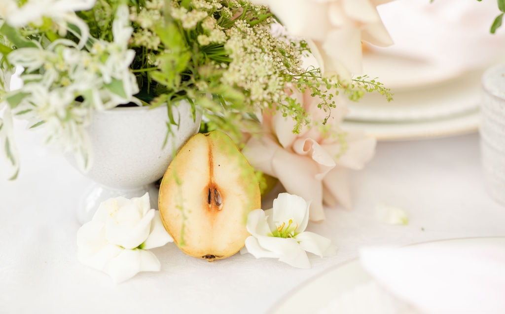 Romantic details of pear halve sitting next to floral arrangement at Denver wedding venue.