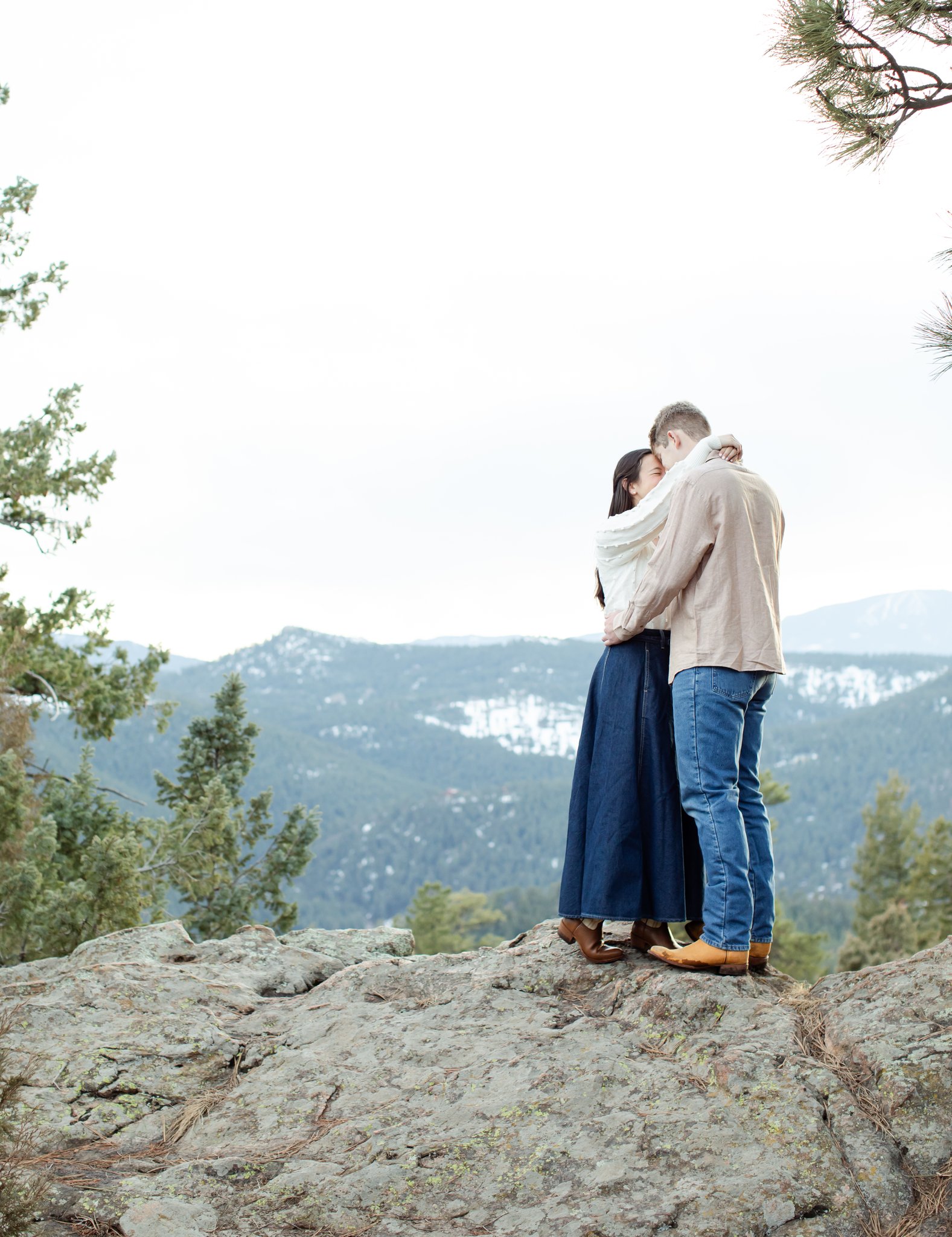 Julia and Jonas on top of a rock with the expanse of mountains the background. They embrace.