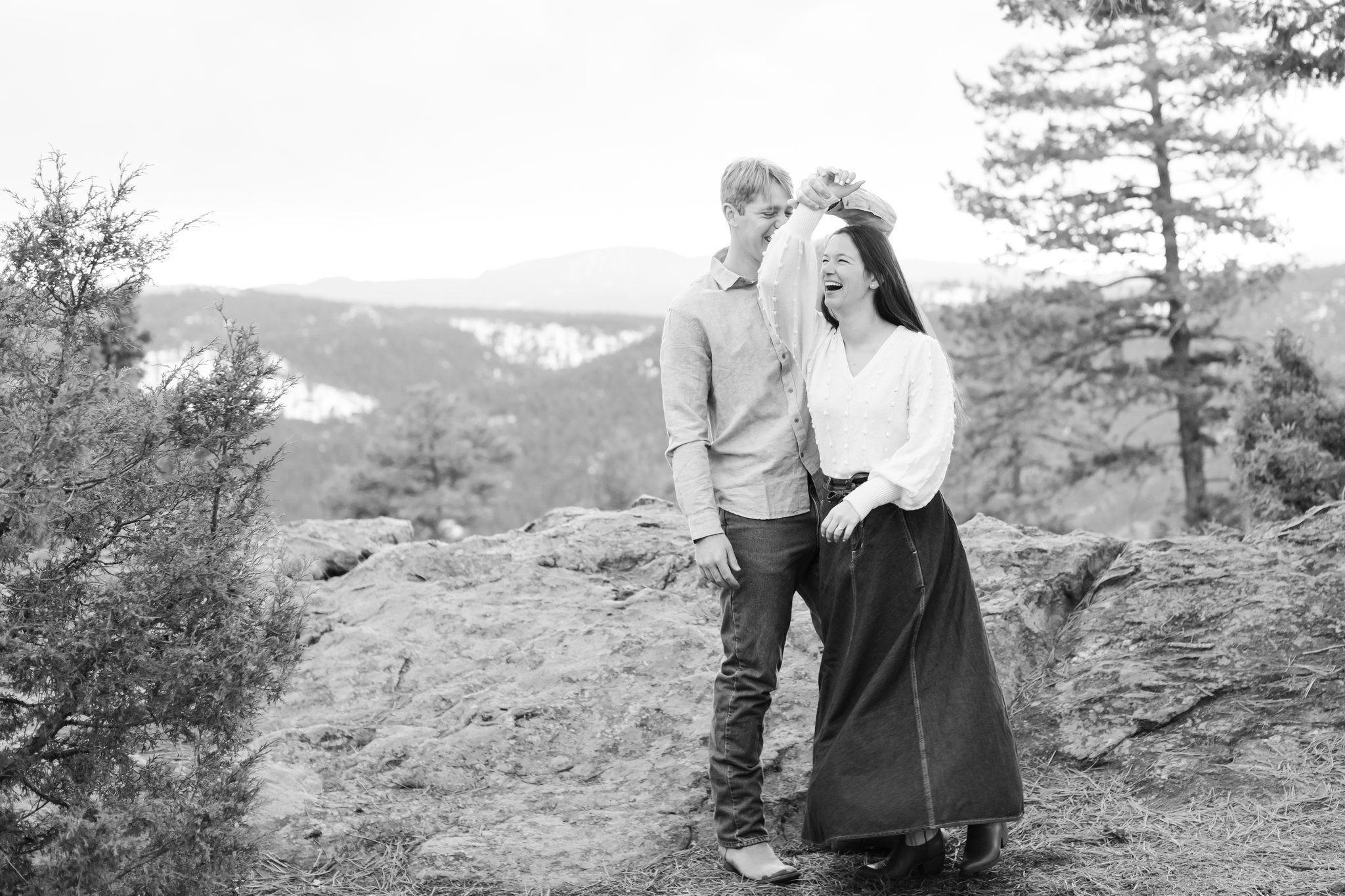 Julia and Jonas dancing near a rock with mountains in the background. She is laughing.