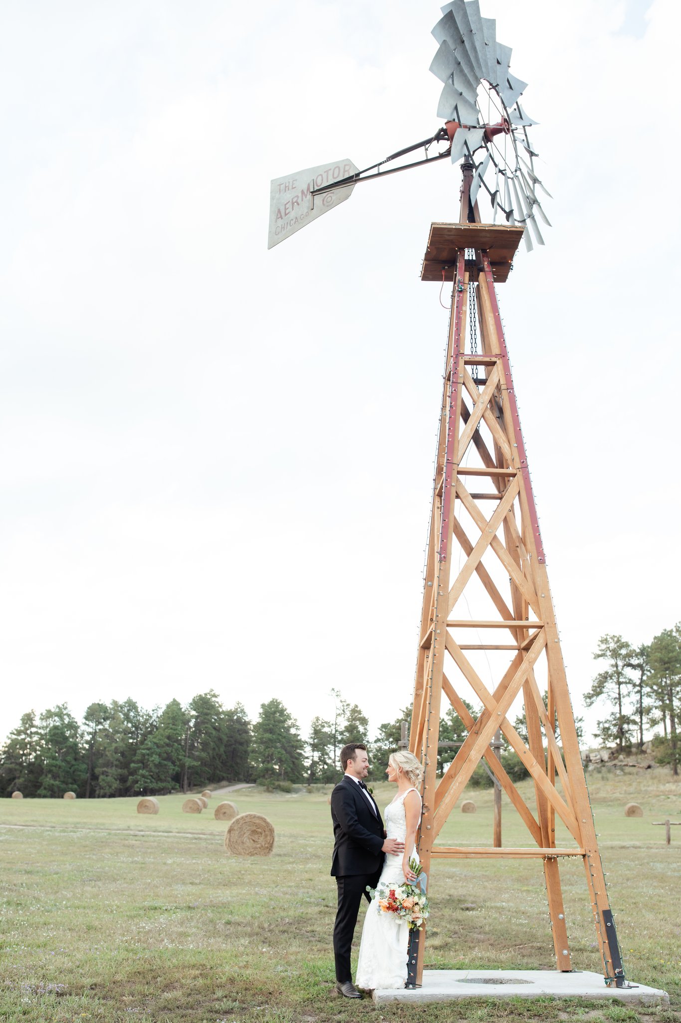 Lauren and Nick lean against a windmill on their wedding day at Younger Ranch in Colorado Springs.