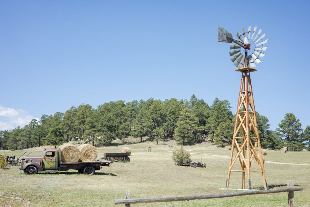 Windmill and rusted vintage truck at Younger Ranch wedding venue. Trees line the background.
