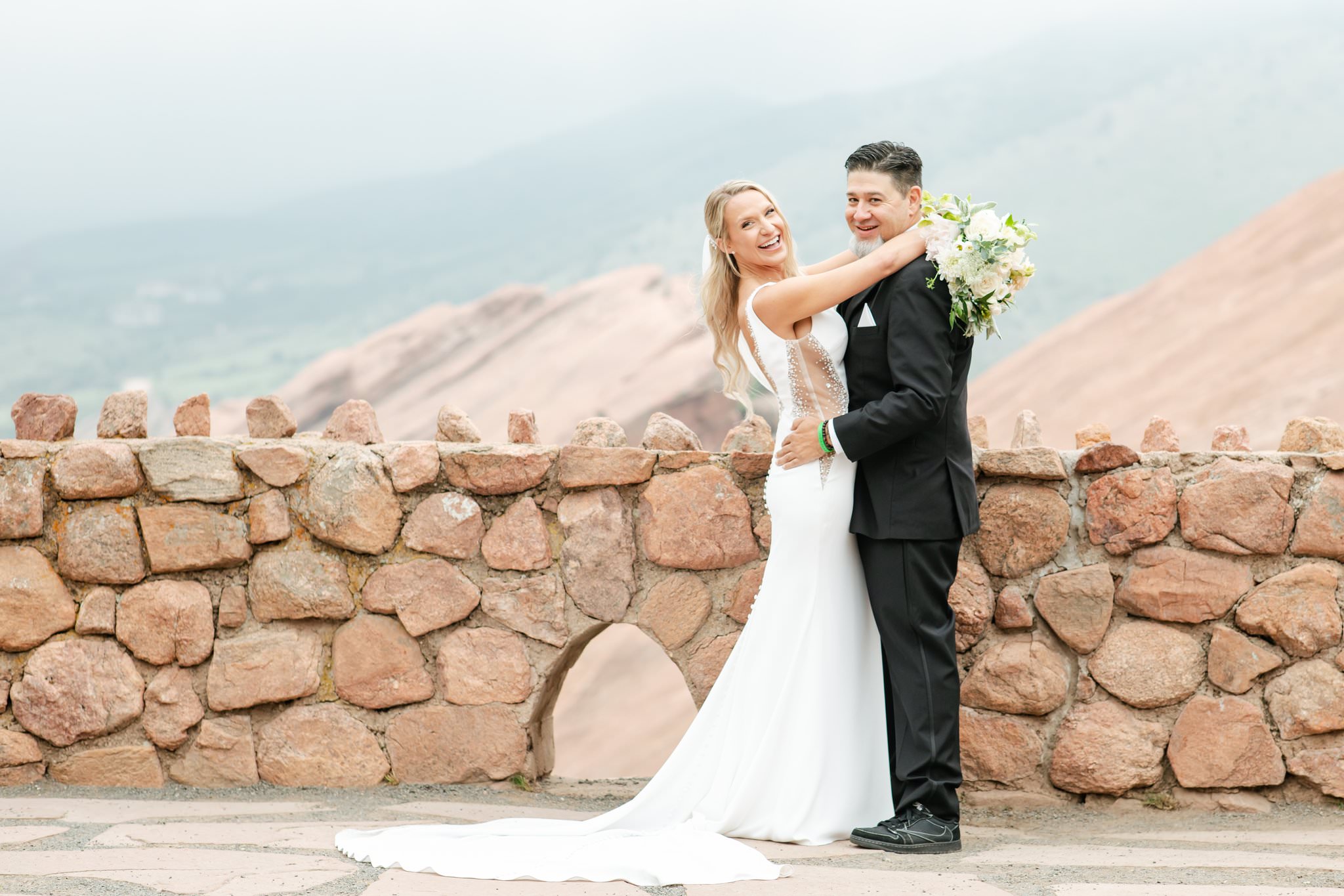 Bride and groom smile toward the camera. Red Rocks park and mountains are behind them.