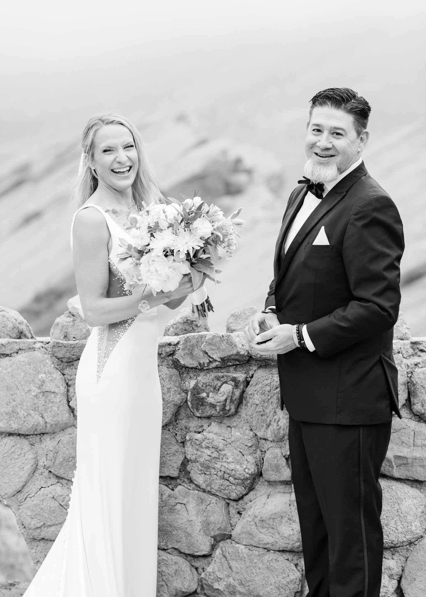 Bride and groom smiling near a rock fence as a show of what is not an AI wedding photo.