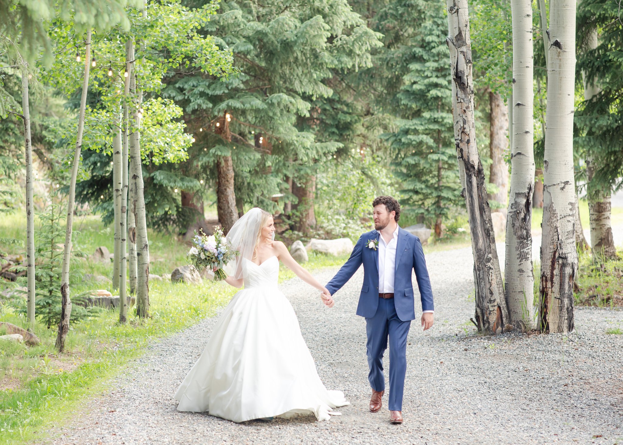 Bride and groom holding hands near river at Blackstone Rivers Ranch wedding venue in the Colorado mountains.