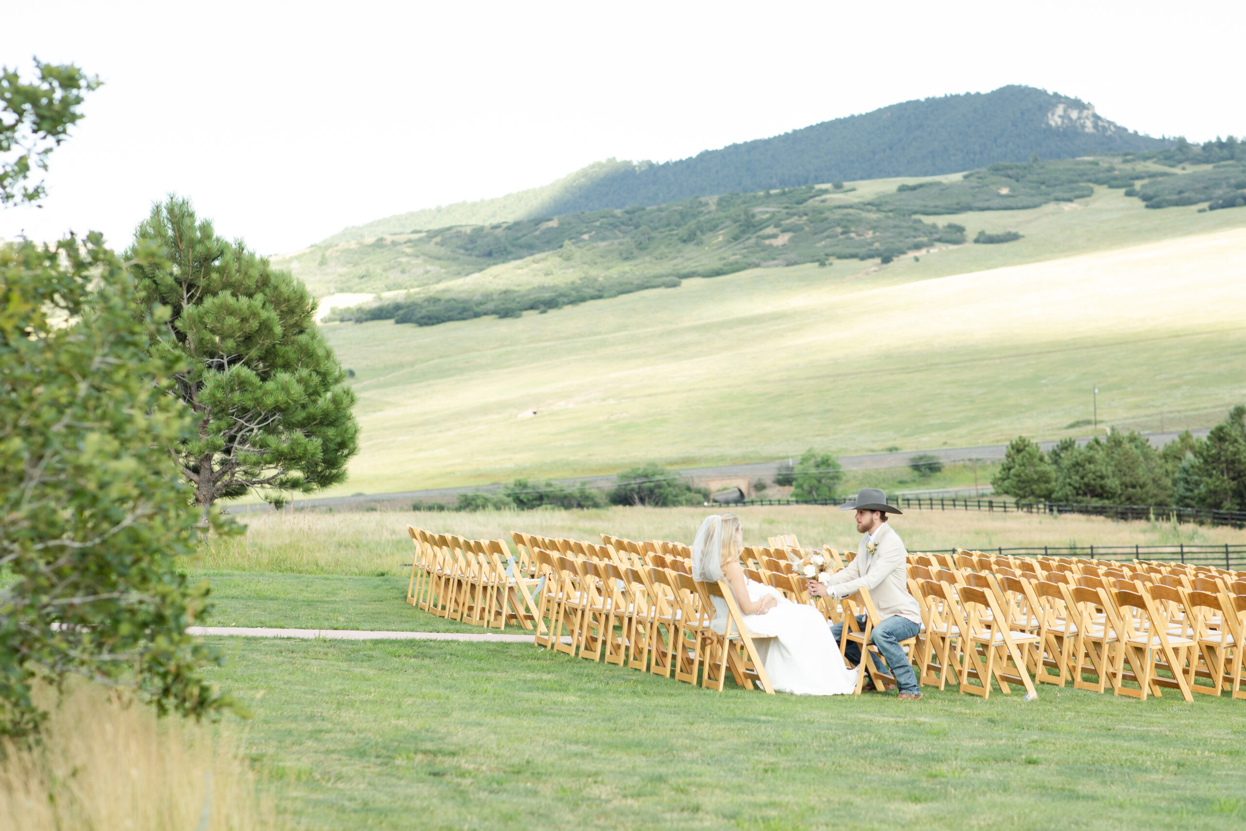 Bride and groom sitting in ceremony seats at their Colorado wedding venue with mountain views. 