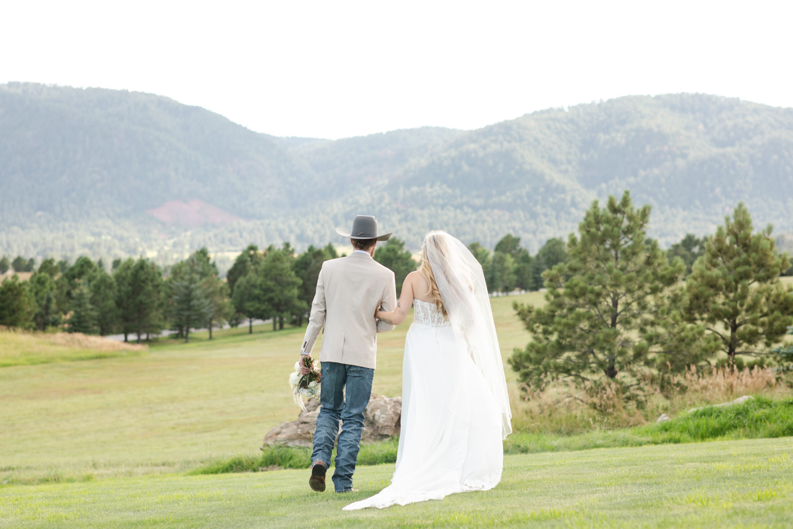 Bride and groom walking through field with mountains nearby in Colorado Springs.