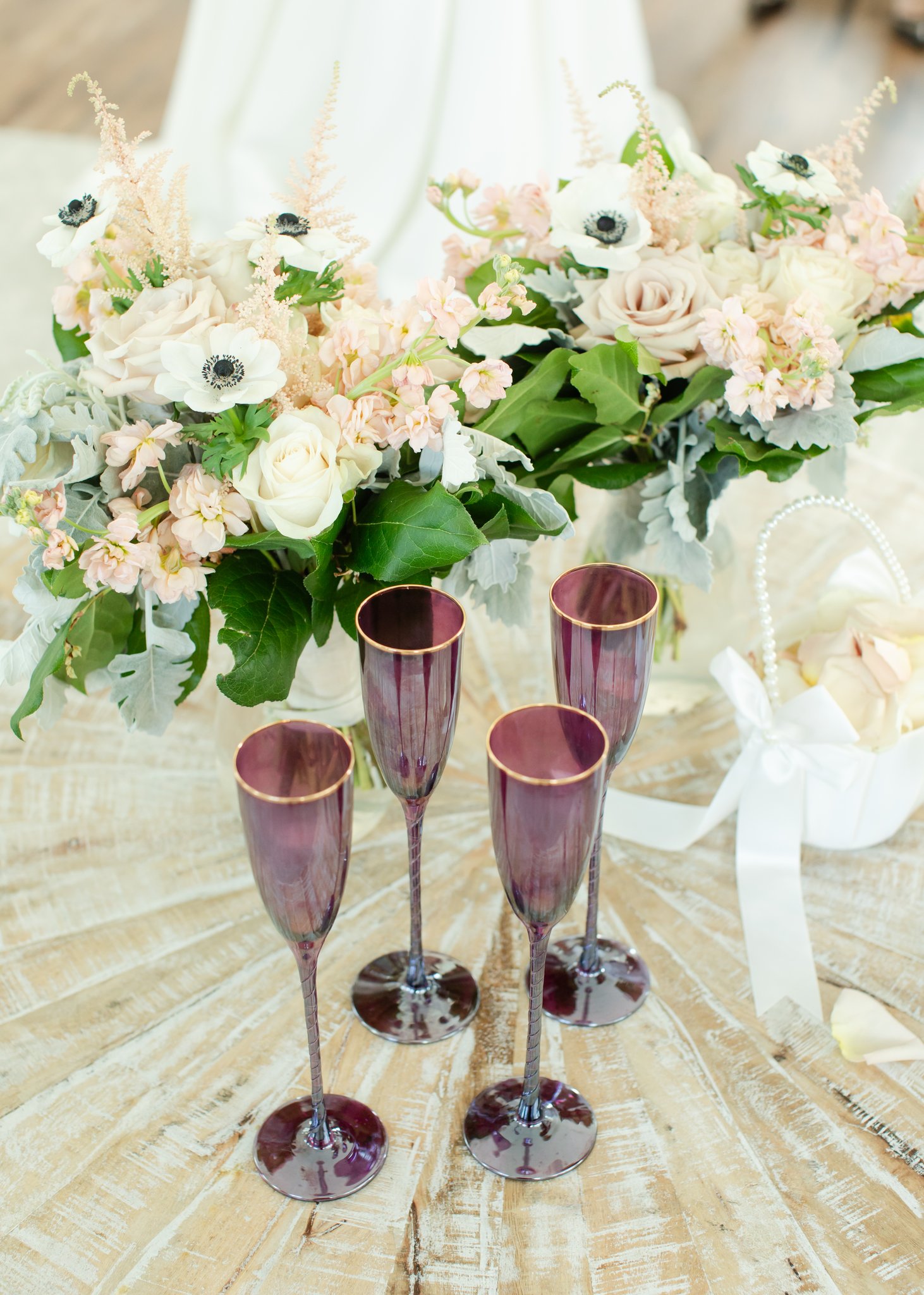 Four plum colored wine glasses sit near wedding bouquets to show details of a wine wedding venue in Colorado.