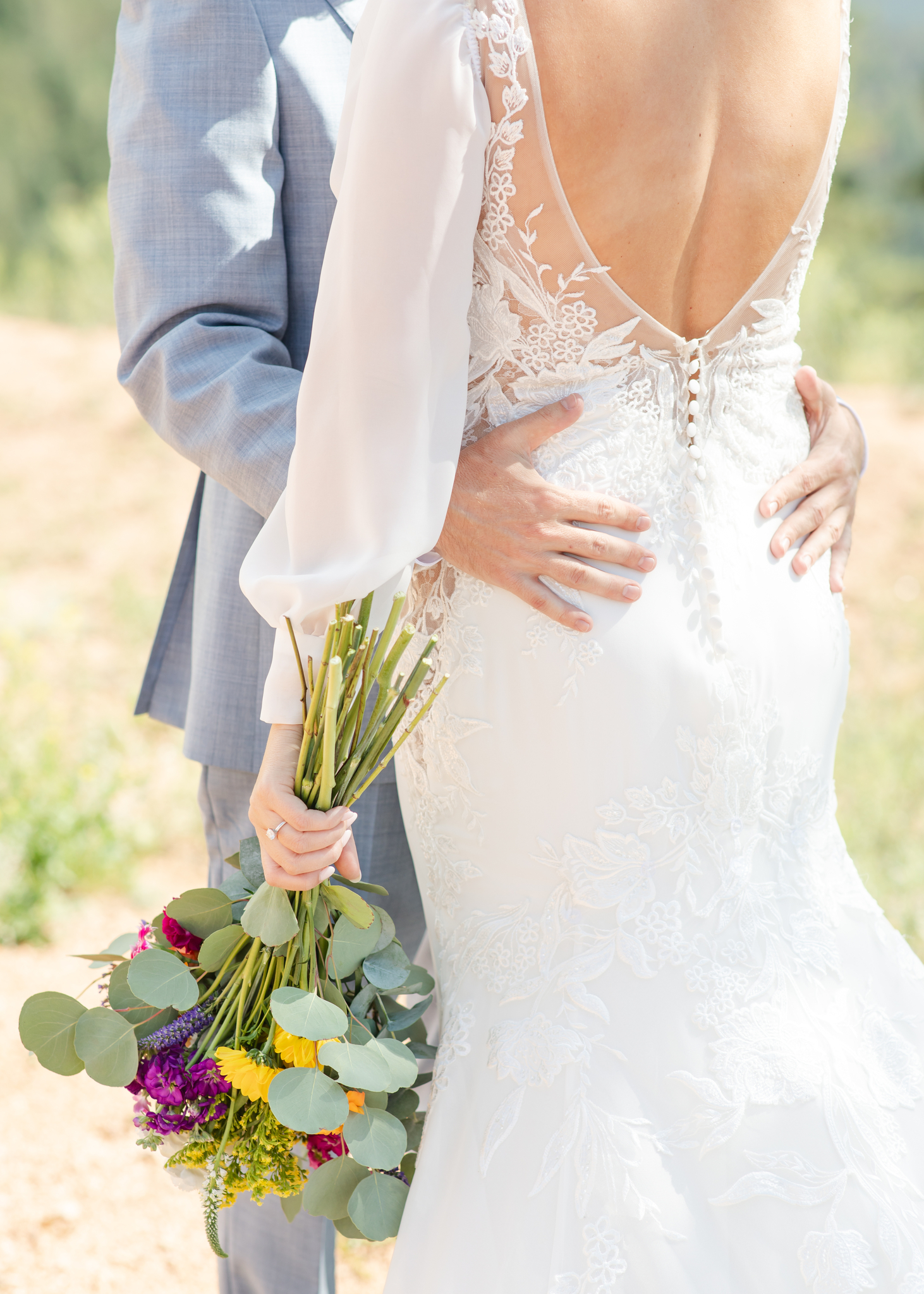 Photo of groom's hands on back of bride as she holds her bouquet at their mountain wedding venue in Woodland Park, Colorado.