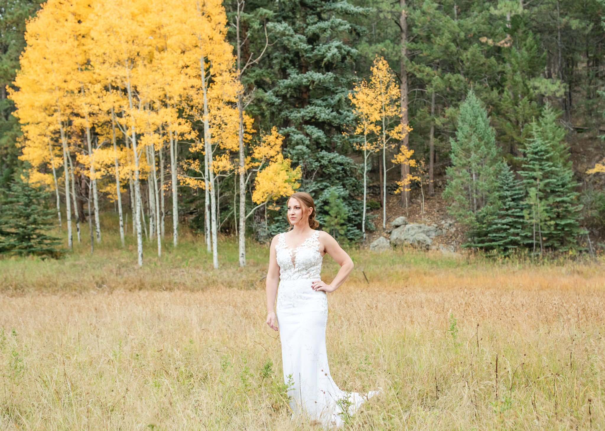 Bride standing with a hand on her hip by golden aspen trees during fall in Colorado.