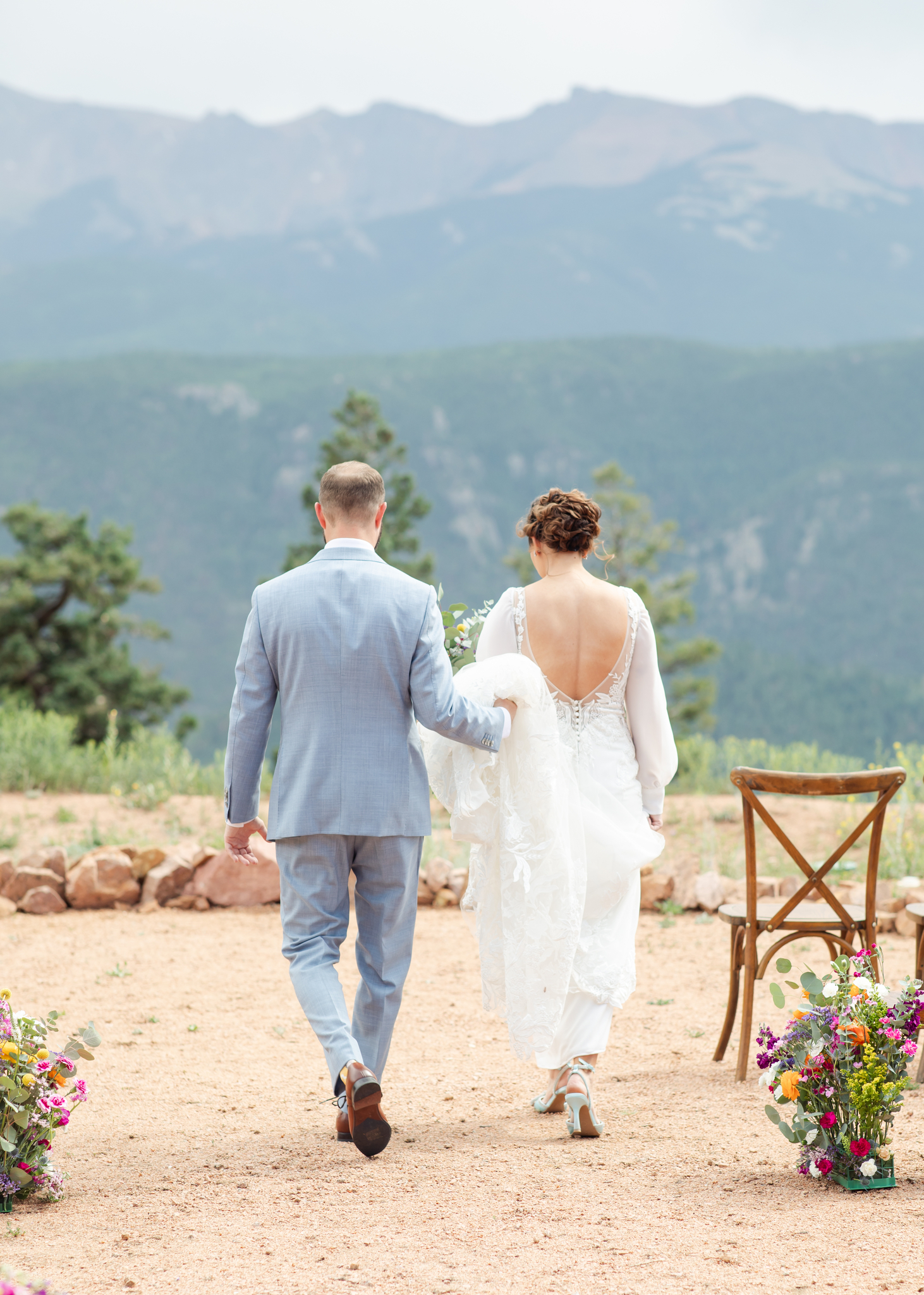 Groom holding bride's train as they walk down aisle in Colorado Springs wedding.