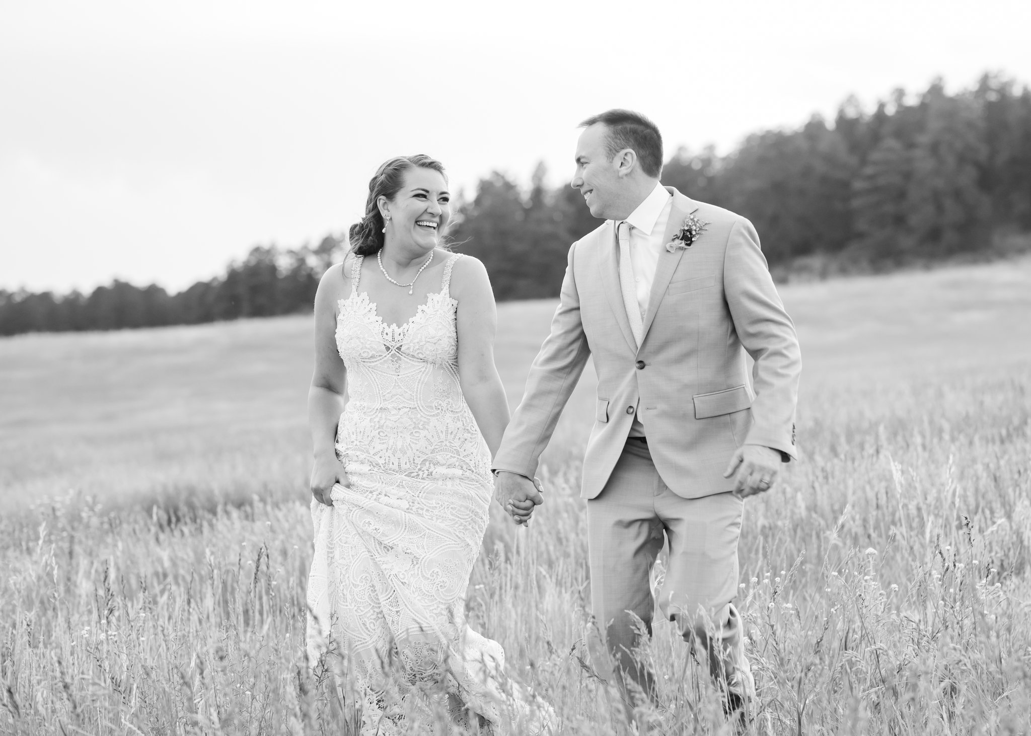 Bride and groom running through field in a black and white timeless wedding photography image.