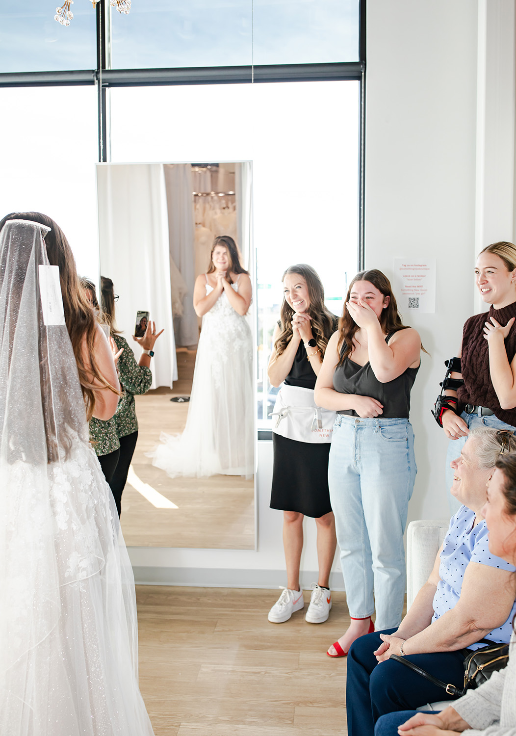 Women covering their mouths as they see a bride trying on a wedding dress at a Denver bridal boutique.