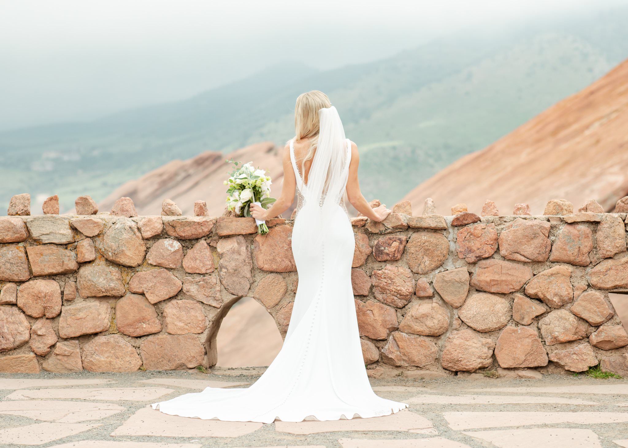 A bride lens on a stone wall with her bouquet after enjoying support from Calluna Events