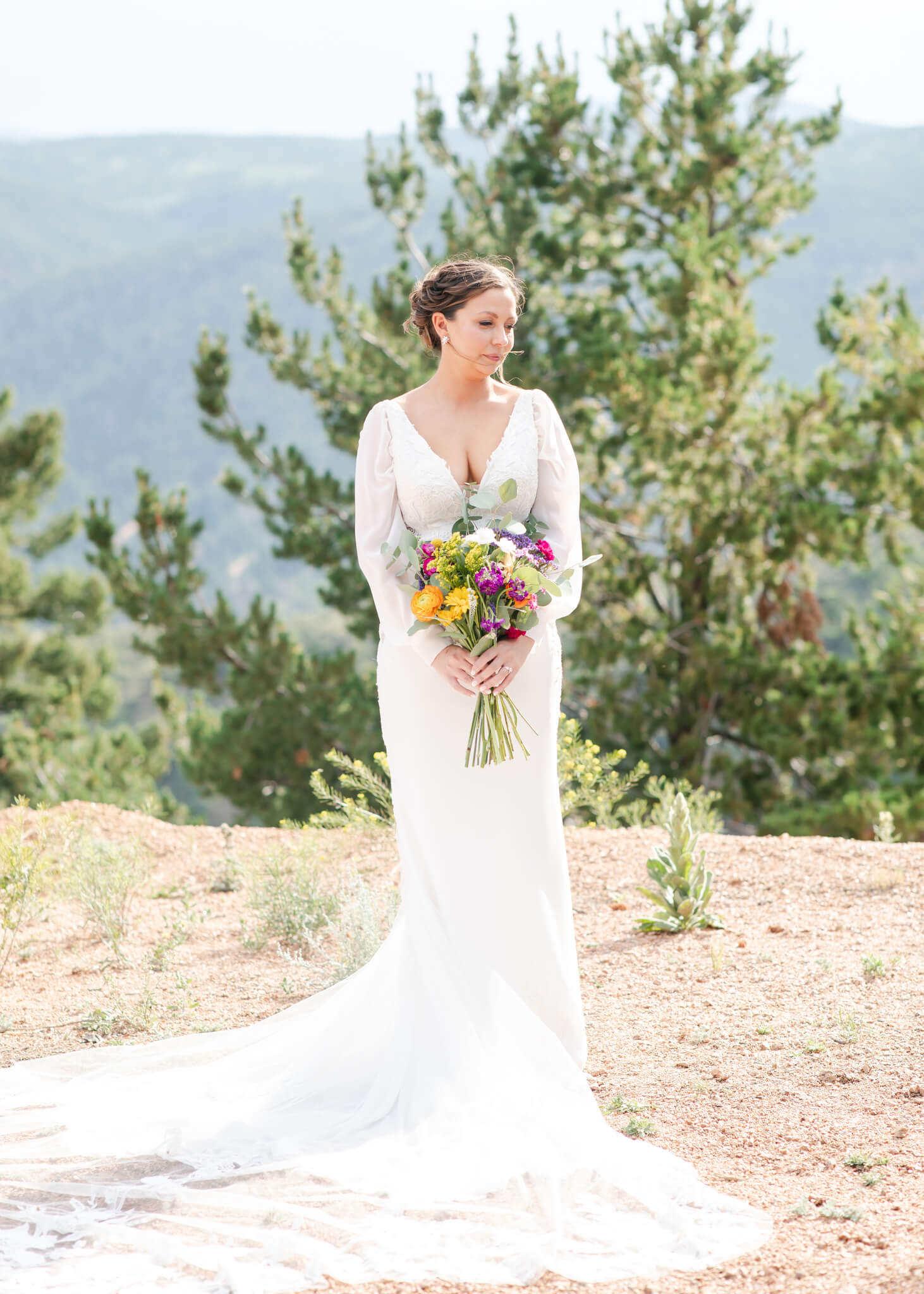 A bride stands in her long gown on a mountain overlook holding her bouquet after thanking Table 6 Productions