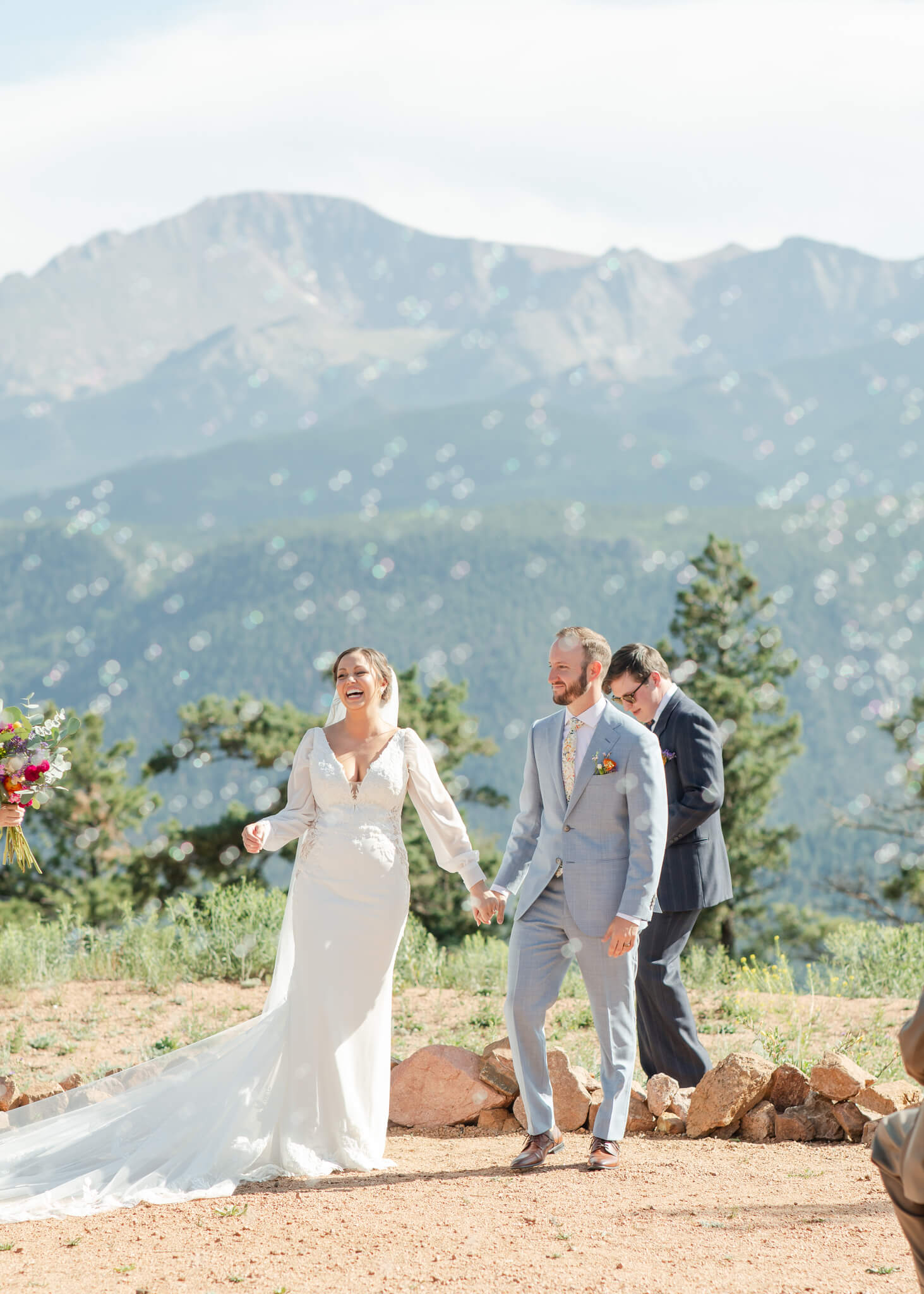 Happy newlyweds smile and hold hands while walking up the aisle of their outdoor ceremony with support from Table 6 Productions