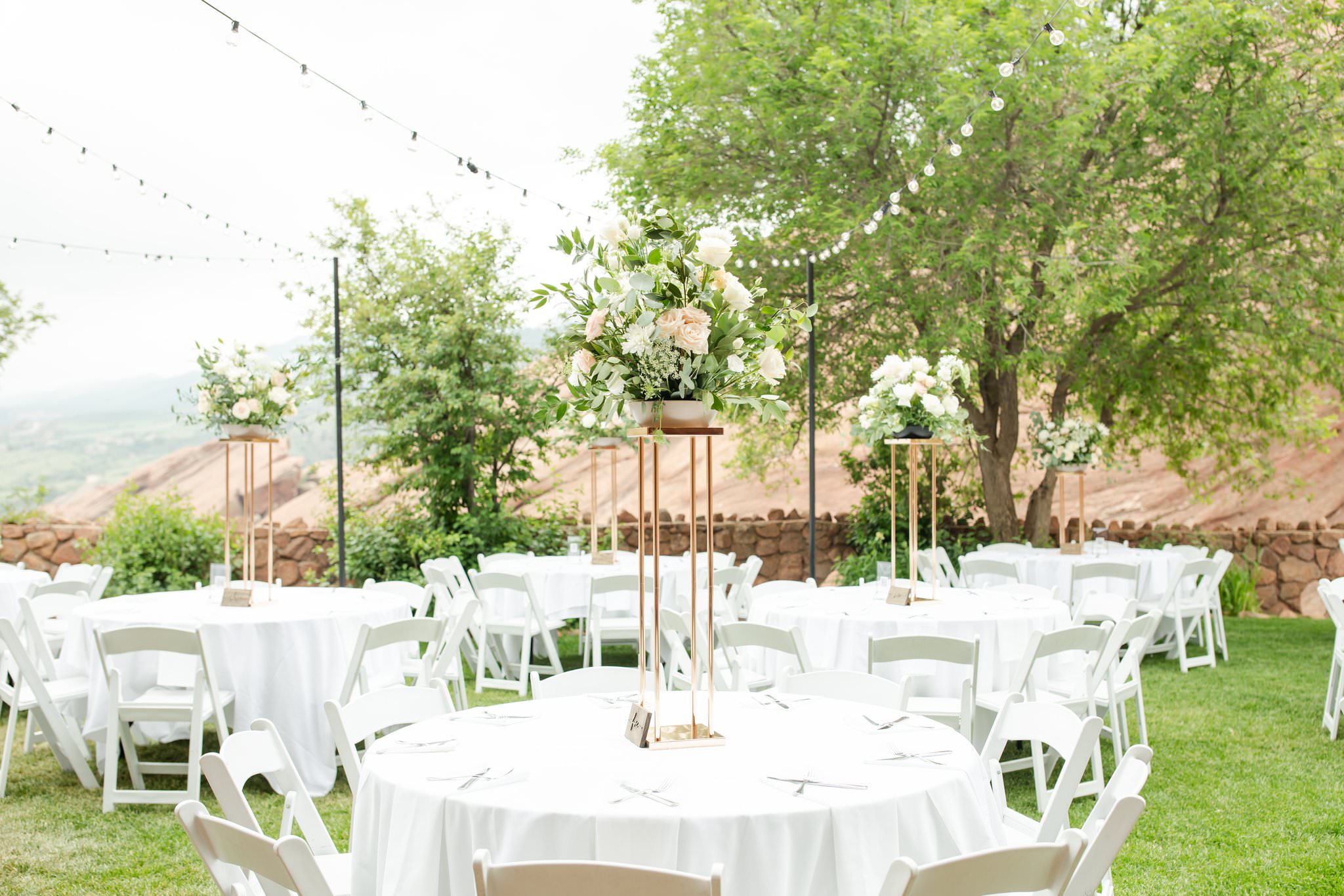 Details of an outdoor wedding reception with white linens and tall floral centerpieces under market lights