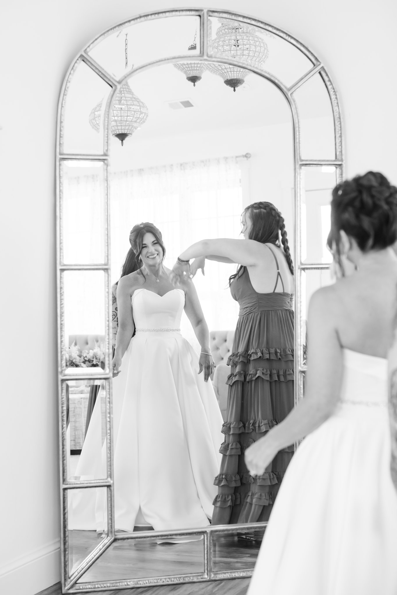 A bride shows off her down in a tall mirror to bridesmaids in a black and white image on her day planned by revel and bloom